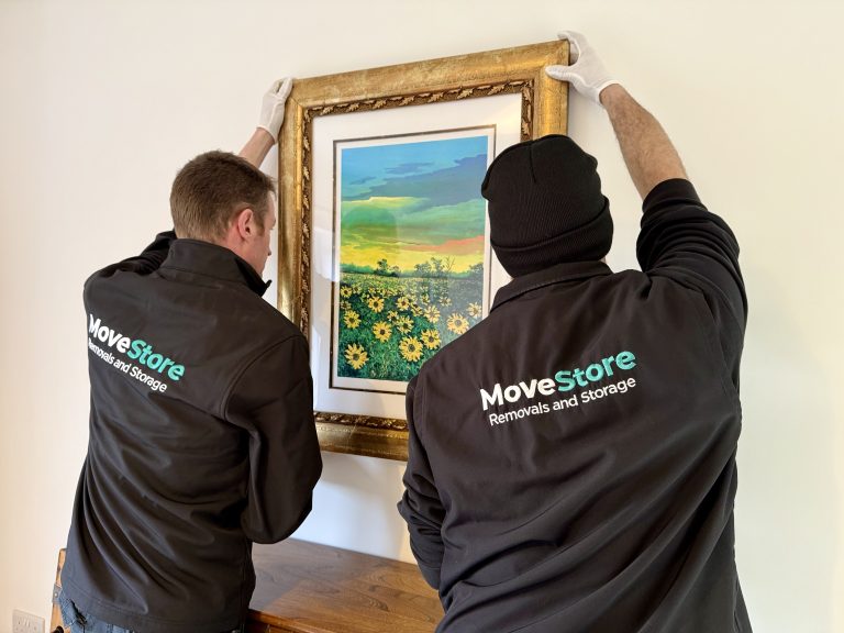 MoveStore movers removing fine art from a wall with white gloves for packing